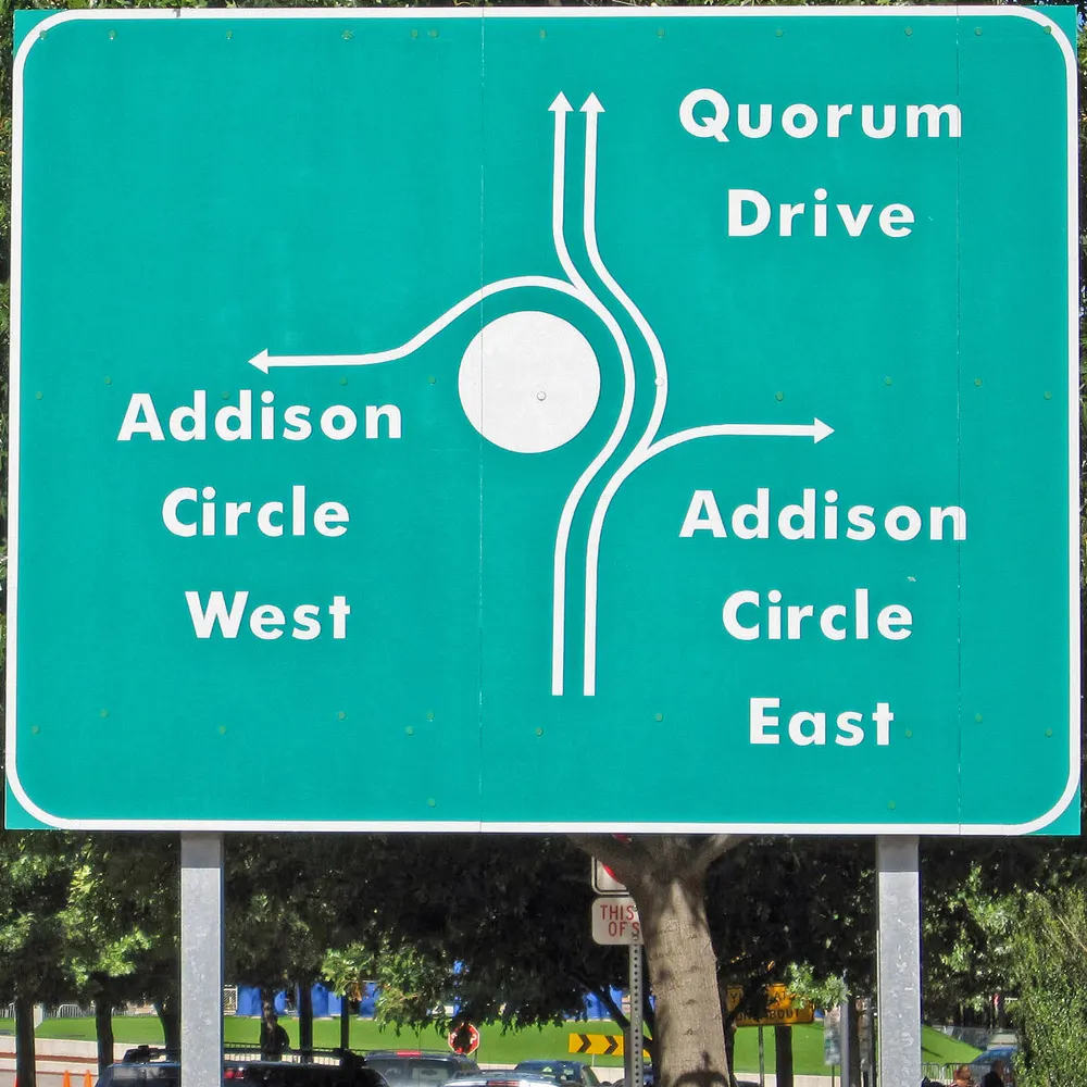Green road sign at Addison Circle roundabout pointing to Quorum Drive and Addison Circle East and West